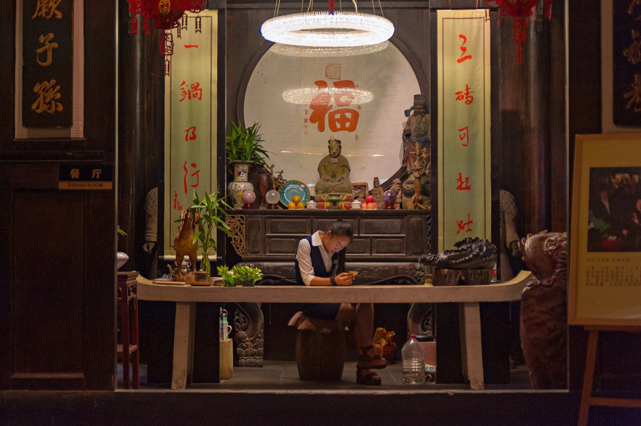 A woman sits in a traditional Chinese interior, engaged with her phone, surrounded by cultural decor.