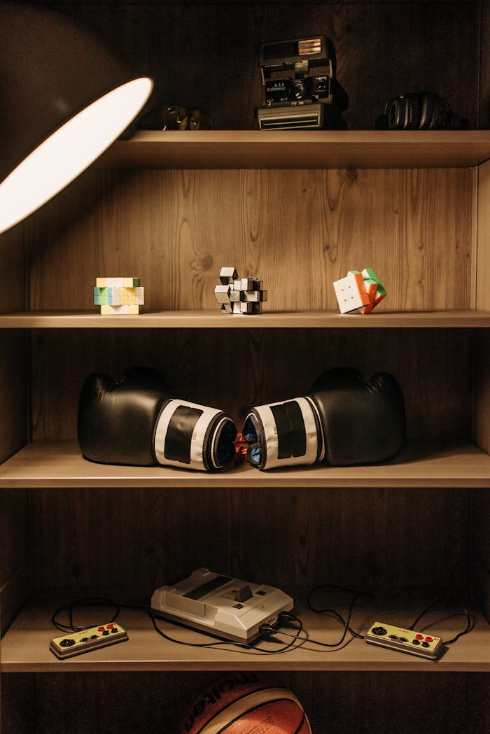 A nostalgic mix of boxing gloves and retro gaming consoles on wooden shelves.